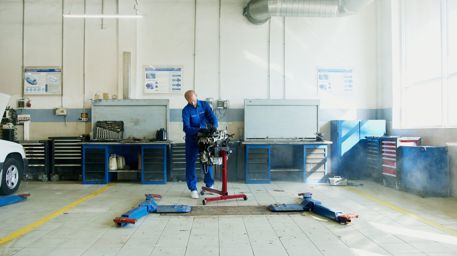 Mechanic in blue uniform working on engine with hydraulic lift in automotive repair shop