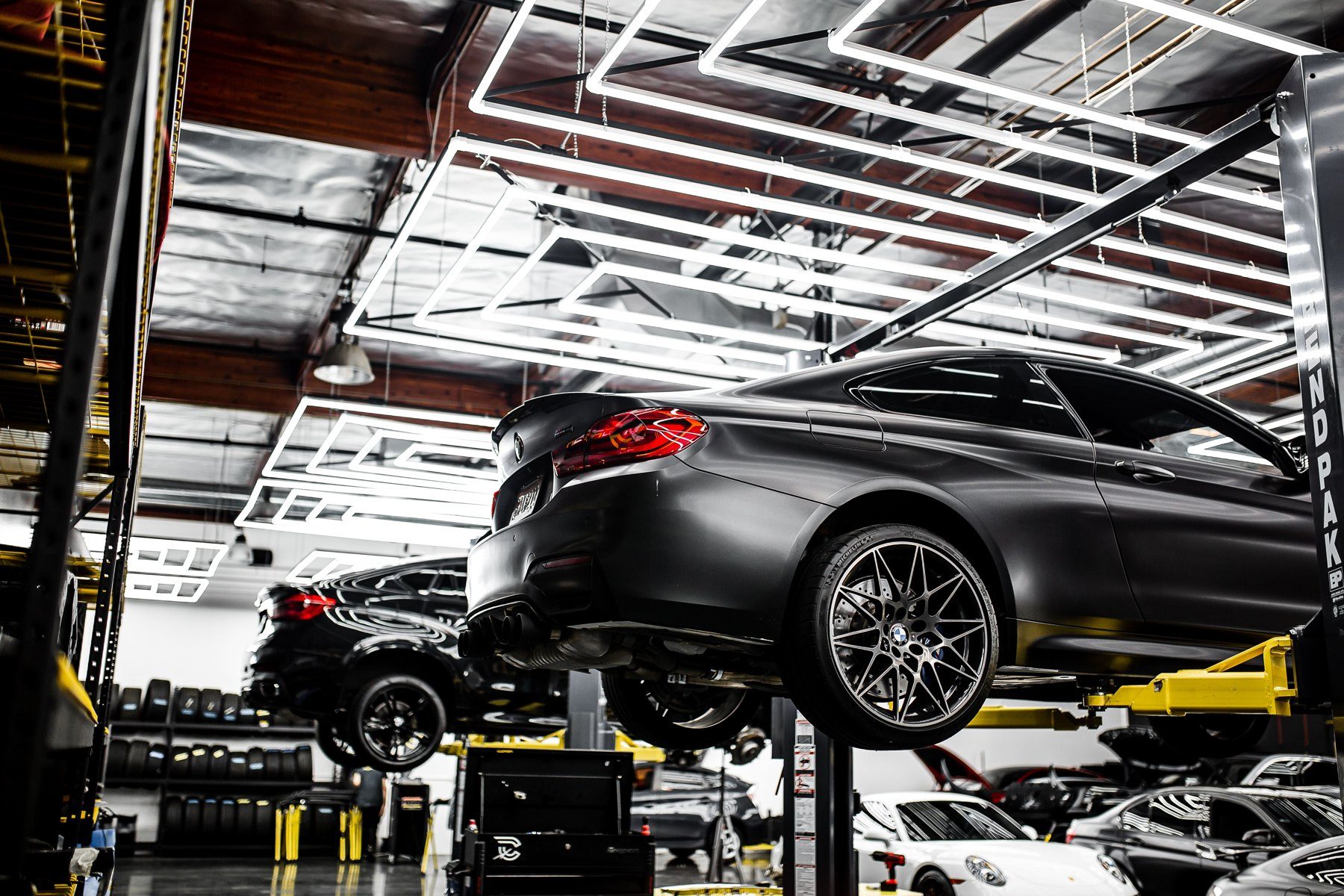 Black sport car on yellow hydraulic lift in modern automotive service facility with bright ceiling lights